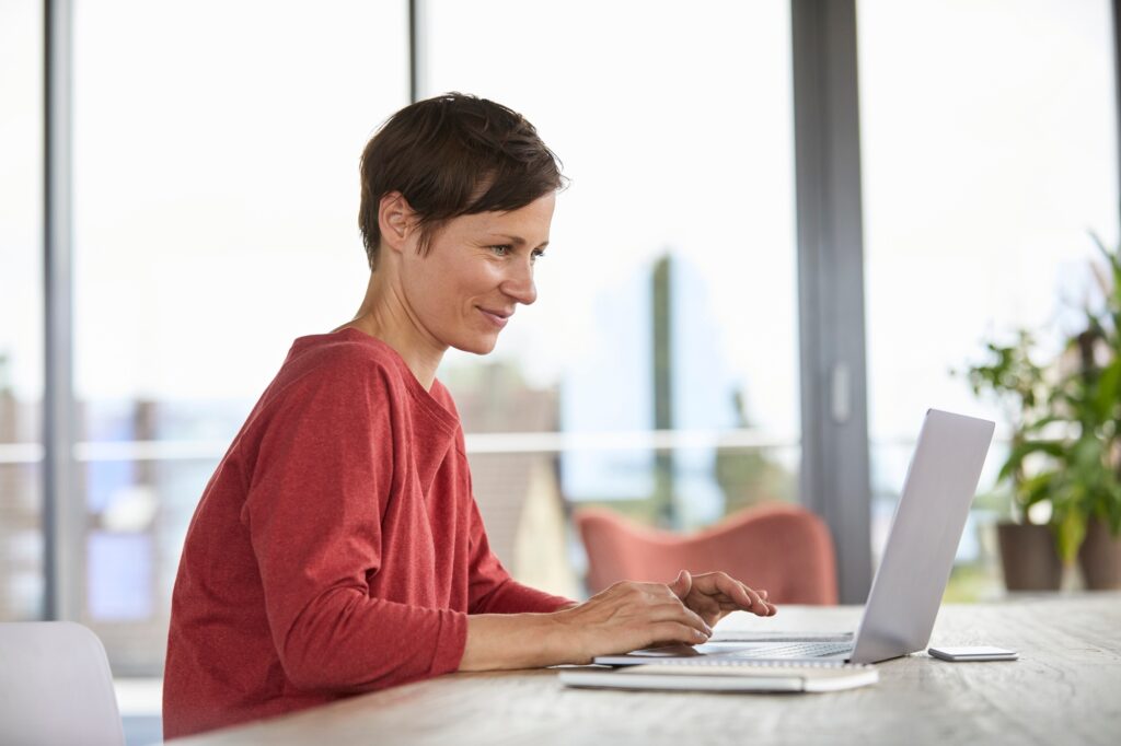 Smiling woman sitting at table at home using laptop